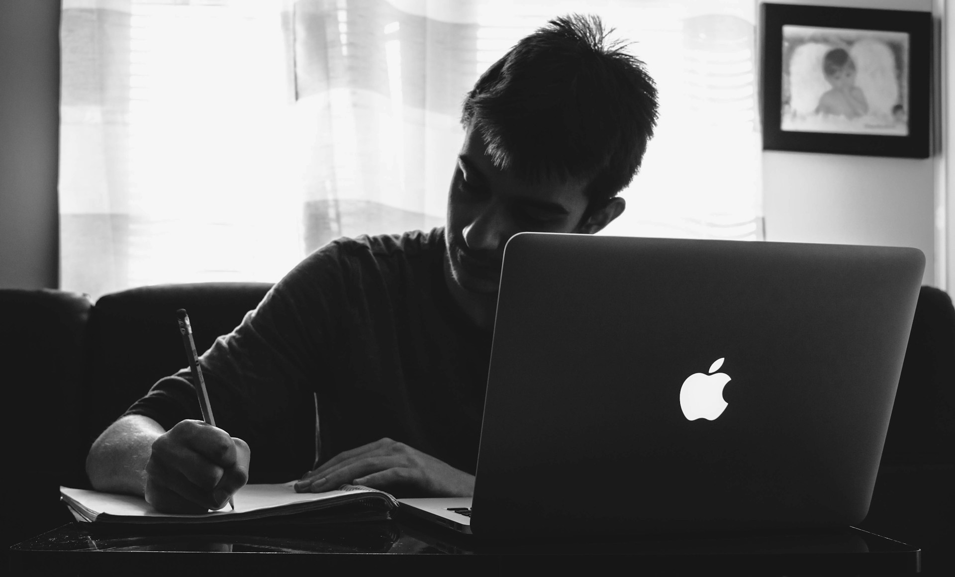 student at a laptop writing in a notebook